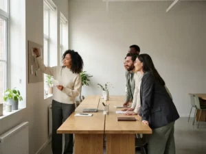 Diverse colleagues collaborating around an oak table in a sunlit open-plan office, one person pinning a note to a communal board.