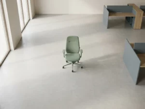 Une chaise ergonomique placée au centre d'un espace de bureau minimaliste, baigné de lumière naturelle grâce à des baies vitrées allant du sol au plafond, avec un espace vide et des agencements de bureaux géométriques en arrière-plan.