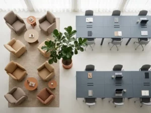 Open-plan office with soft armchairs in a lounge corner beside a structured hot-desk grid, bridged by a potted plant, in slate grey and warm sand tones.