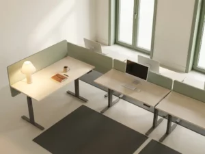 Un bureau en open space où, parmi les tables vides, un bureau baigné d'une lumière chaleureuse est occupé par un ordinateur portable et une tasse de café ; la douce lumière du matin pénètre à travers les baies vitrées.